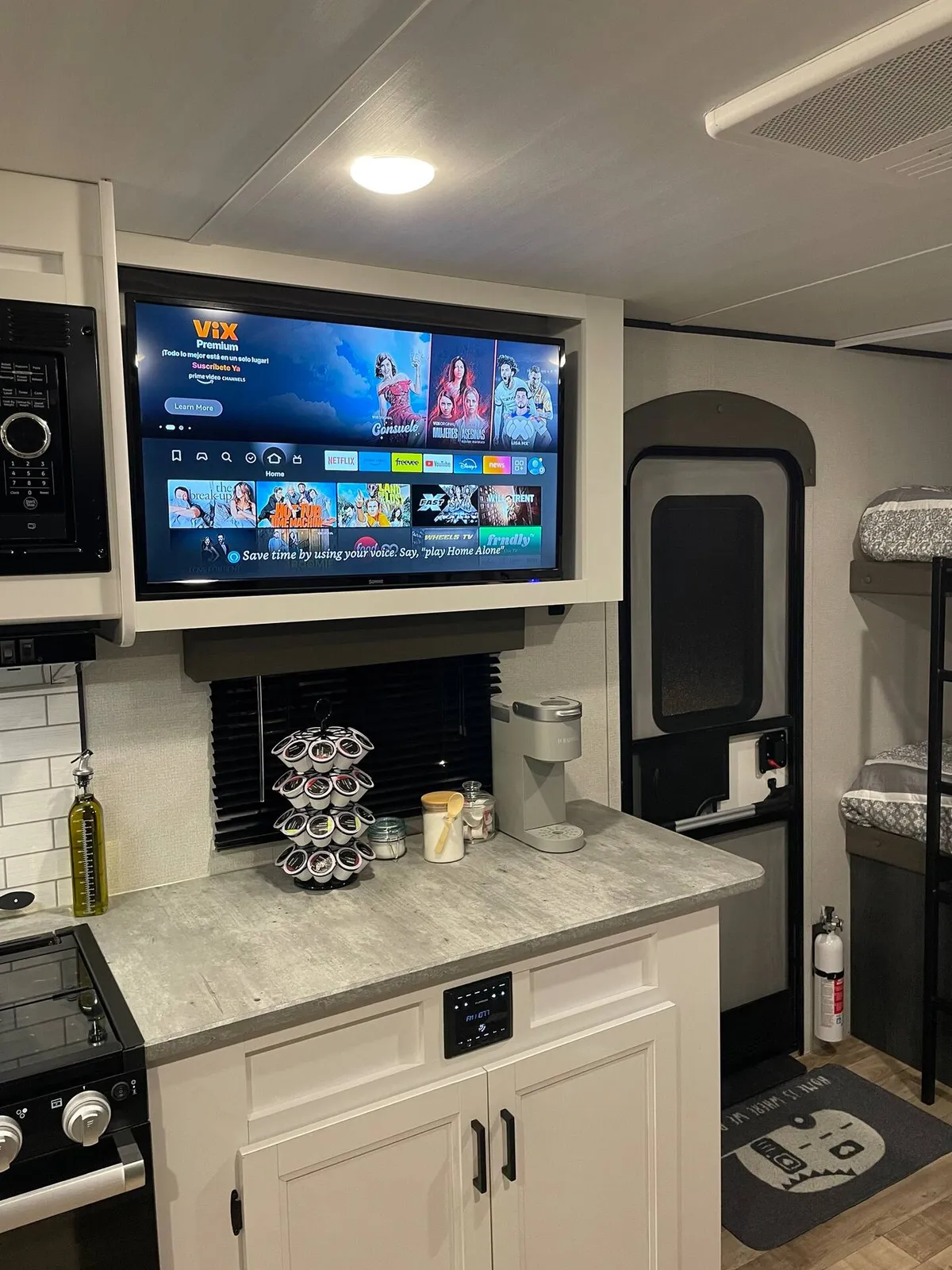 A portion of the RV's living space with a television displaying streaming options, a coffee machine on the kitchen counter, and a stove. The area invites relaxation and entertainment, making it suitable for movie nights or preparing snacks and drinks together.