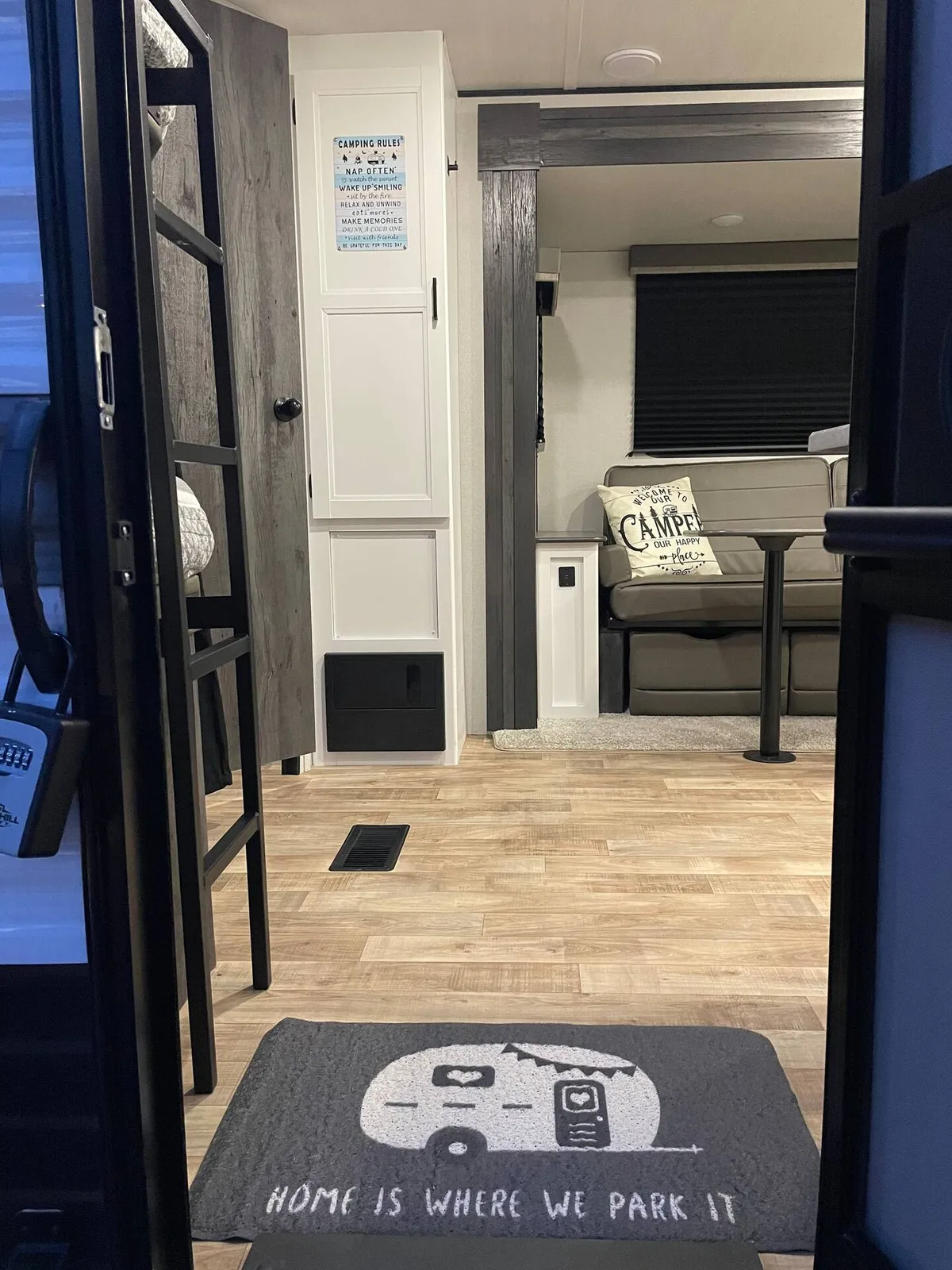 This interior scene features a welcoming entry with a 'camping rules' sign and a cozy seating area, with the focal point on inviting full-size bunk beds. The space is designed for relaxation, socializing, and napping, evoking memories of cozy evenings and playful moments.