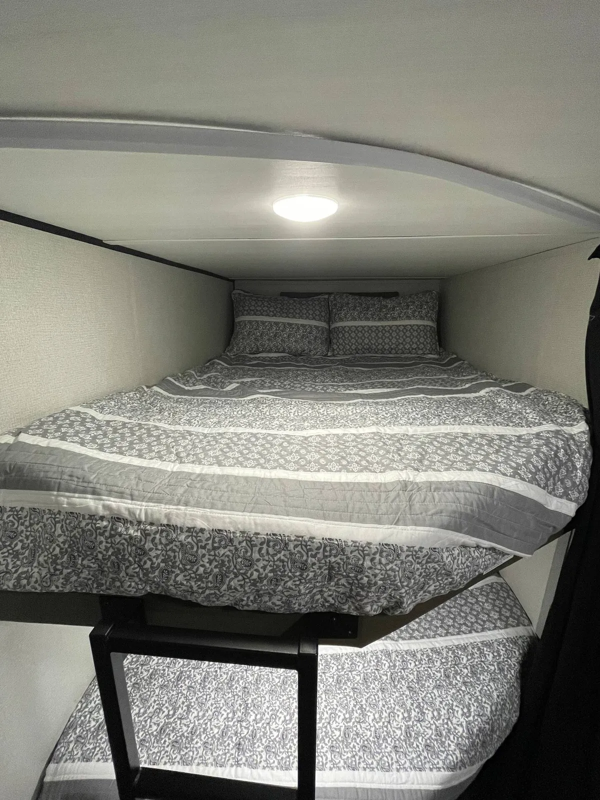 A close-up of a bunk bed structure with crisp bedding and a gentle light fixture, creating an intimate nook for sleeping, reading, or relaxing. The atmosphere is peaceful and private, making it perfect for quiet moments or bedtime routines.