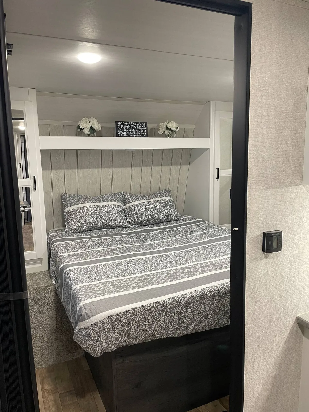 An interior shot showing a queen bed adorned with soft bedding, a decorative sign, and shelves with flowers. The setting is calm and welcoming, ideal for unwinding, reading, or enjoying a restful sleep after an active day.