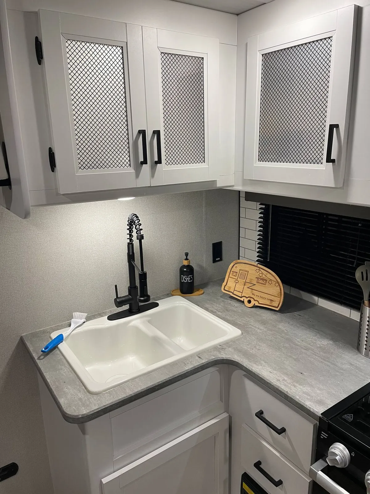 This image showcases a well-equipped RV kitchenette with a sink, countertop, kitchen cabinets, faucet, and a cutting board. The setting is inviting and modern, suggesting a family-friendly environment where meals can be easily prepared and enjoyed together.